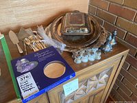 Wide view of the silver plated items including cutlery, cake servers, salt and pepper shakers and serving platters arranged on a wooden sideboard.