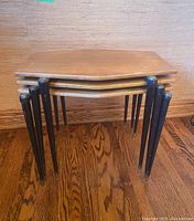 Three tables nested together, profile view showing stacking arrangement and leg design.