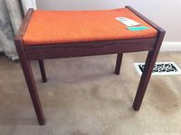 Angle view of wooden stool with orange upholstered seat showing condition and overall structure.