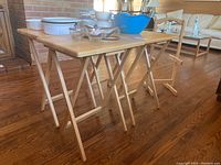 Four folding wooden tray tables set up side by side on a hardwood floor, some kitchenware items on top which are not included.