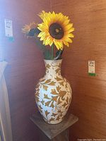 Full view of Italian ceramic vase with faux sunflowers inside. Vase is white with gold leaf pattern and sunflowers have bright yellow petals.