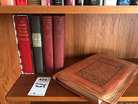 Books arranged on wooden shelf in a row showing covers and spines, including Shakespeare slipcased book, three history of art books, and a leather bound book.