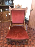 Front view of vintage carved wood chair upholstered in rust fabric, showing detailed top crest and seat.