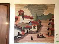 Full view of the wall hanging depicting a village with houses, mountains, and figures in traditional clothing.