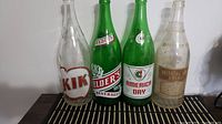 Front view of all four soda pop bottles standing side by side on a dark surface with a light background.