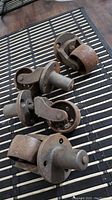 Four old cast iron castor wheels laid out on a striped surface, showing their full body and mounting ends.