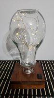 A large glass bulb shaped lamp with LED string lights inside on a wooden base with power switch.