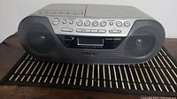 Front view of gray Sony boombox showing speakers, cassette deck, CD playback, and control buttons.