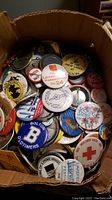 Box of assorted vintage button pins showing various political, festival, school, and organizational designs.