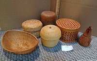 Photo shows six wicker items: five containers with lids and one open shallow basket. The tall container has coasters inside. One container is shaped like a chicken, identified as a garlic basket.