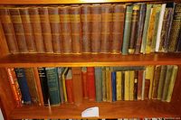 Full bookshelf view showing 12-volume Dickens set with heavily worn leather bindings and a range of other older books beneath.