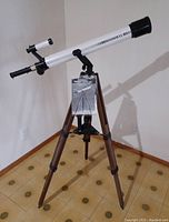Full view of Bushnell Banner Astro 280 telescope mounted on wooden tripod stand with manual hanging on the stand.