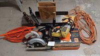 Photo showing 2 orange extension cords, Black & Decker circular saw, Black & Decker 5 in 1 sander in box, wooden and metal hand planes, hand brace drill, and a wooden box with small parts.