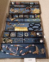 Overhead image showing multiple compartments with assorted costume jewelry including necklaces, earrings, bracelets, pins and brooches arranged on blue fabric background.