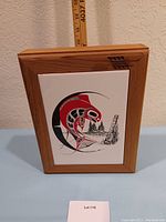 Front view of ceramic tile artwork and cedar box, showing the inset tile with Indigenous style artwork and measurement scale behind.