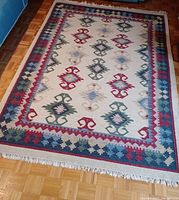 Full view of the large woven area rug displaying its geometric pattern and multicolored border on a wooden floor.