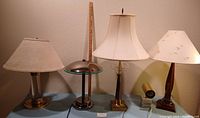 Five lamps displayed on table including four table lamps with different bases and shades plus one small flood light with marble base
