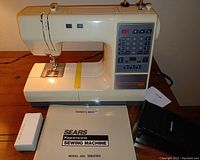 Sears Kenmore sewing machine Model 385 with control panel, digital display showing stitch number 10, masking tape on the base, and power cord. Owner's manual and foot pedal also present.