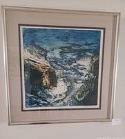Framed lithograph titled "Ocean" showing blue and brown abstract oceanic scene, housed in a silver metal frame with white matting.