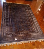 Full view of light blue Bukhara rug with geometric motif and fringe on hardwood floor