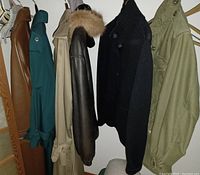 Photo showing five vintage outerwear items hanging on a rack including leather coats, trench coats, a heavy sweater jacket, and an army green jacket.