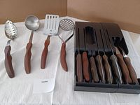 Full view of vintage cooking utensils with wooden handles and cutlery set in a black knife tray.