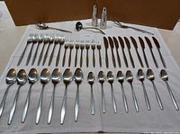 Complete flatware set laid out on cloth including forks, knives, spoons, serving pieces, and salt & pepper shakers.