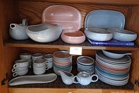Upper cabinet shelf with oval platters in coral and glacier blue, shallow serving bowl and coffee pot