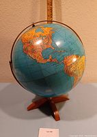 Image shows a vintage student desk globe on a wooden tripod stand, highlighting geographic details of North and South America.