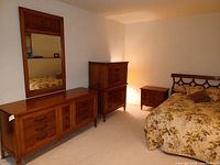Wide view showing dresser, highboy, nightstand, headboard and mirror arranged in bedroom.
