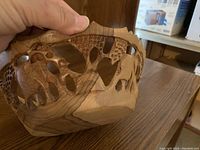 Hand holding side view of carved wooden elephant bowl, showing cut-out elephant shapes and wood grain patterns.