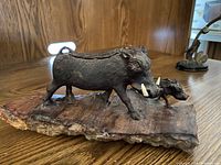 Front and side view of two wooden carved African warthogs mounted on a wooden platform, showing the intricate details of the tusks and fur texture.
