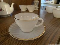 Teacup with matching saucer showing gold trim around rims and scalloped edge on saucer.