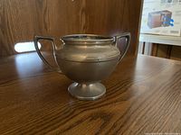 Silver-colored small pot with two handles on wood surface