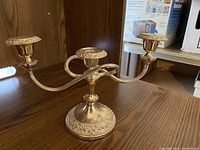 Silver three-arm candelabra with detailed ornate base, holding three candles, placed on a wood surface