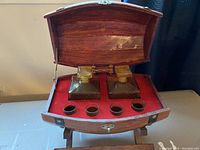 Wooden cask with two square glass decanters and four shot glasses inside red felt lining.