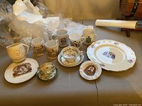 Photo showing assorted royal memorabilia including commemorative mugs, plates, teacups, saucer and ashtray, laid out on a table with bubble wrap packaging.
