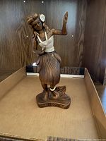 Wooden carved figurine of a dancing girl in a traditional skirt and top, standing on a carved base.
