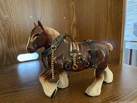 Front side close-up of one ceramic Clydesdale horse showing brown glossy finish and detailed harness with metal chains.