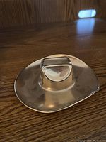 Brass cowboy hat with a unique handle inside, shiny finish, placed on wooden surface