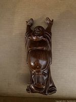 Top-down view of dark polished wooden Laughing Buddha carving showing raised arms and smiling face on plain background.
