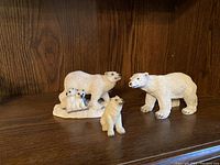 Three small polar bear figurines displayed on a wooden shelf. From left to right: a parent bear with two cubs on a base, a single young polar bear seated in front, and a single adult standing polar bear.