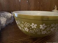 Olive green glass mixing bowl with white flowers and stems on exterior.