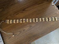 Full length view of beaded tie belt laid flat on wood surface showing cream elongated beads interspersed with smaller round brown beads and silver accent beads.
