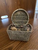 Photo of small new tabletop fountain with circular tiered water spout and basin filled with smooth natural river stones.