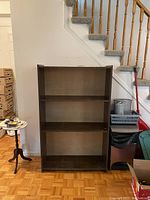Front view of the brown pressboard shelf unit, showing three fixed shelves, no visible marks or damage.