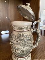 Close-up photo of wooded merganser themed hand-painted ceramic lidded stein with pewter lid and detailed embossed bird design on body.