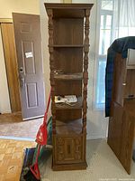 Front view of tall wooden shelf showing three open shelves and decorative bottom door with burned posts.