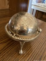 Footed globe style covered ashtray with leaf pattern on dome lid standing on wooden surface
