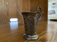 Engraved silver cup with butterfly-shaped handle and decorated surface on wooden table